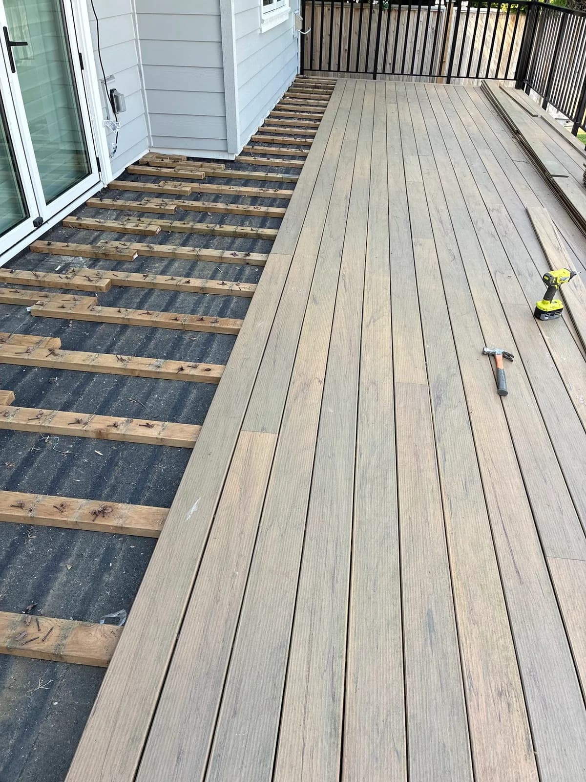 Deck boards partially removed beside a house, exposing the joists underneath