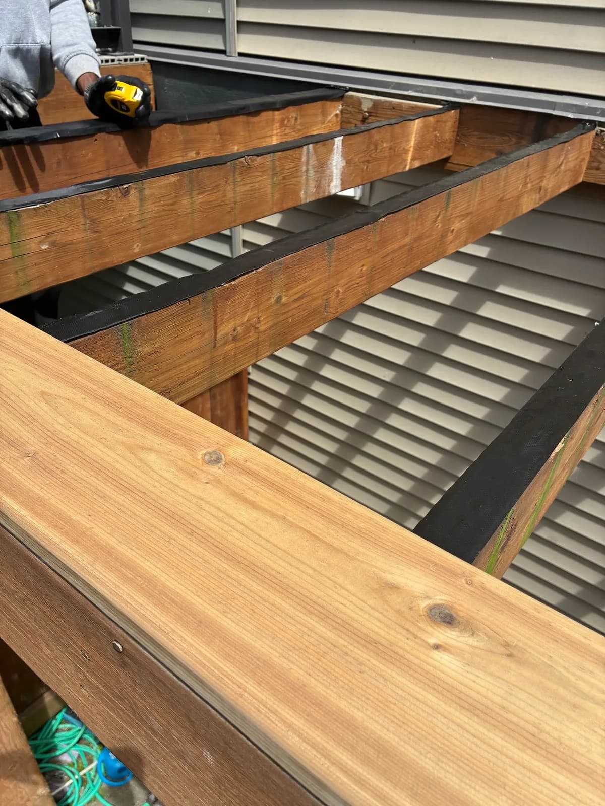 New wood deck boards being fitted over exposed joists beside the house