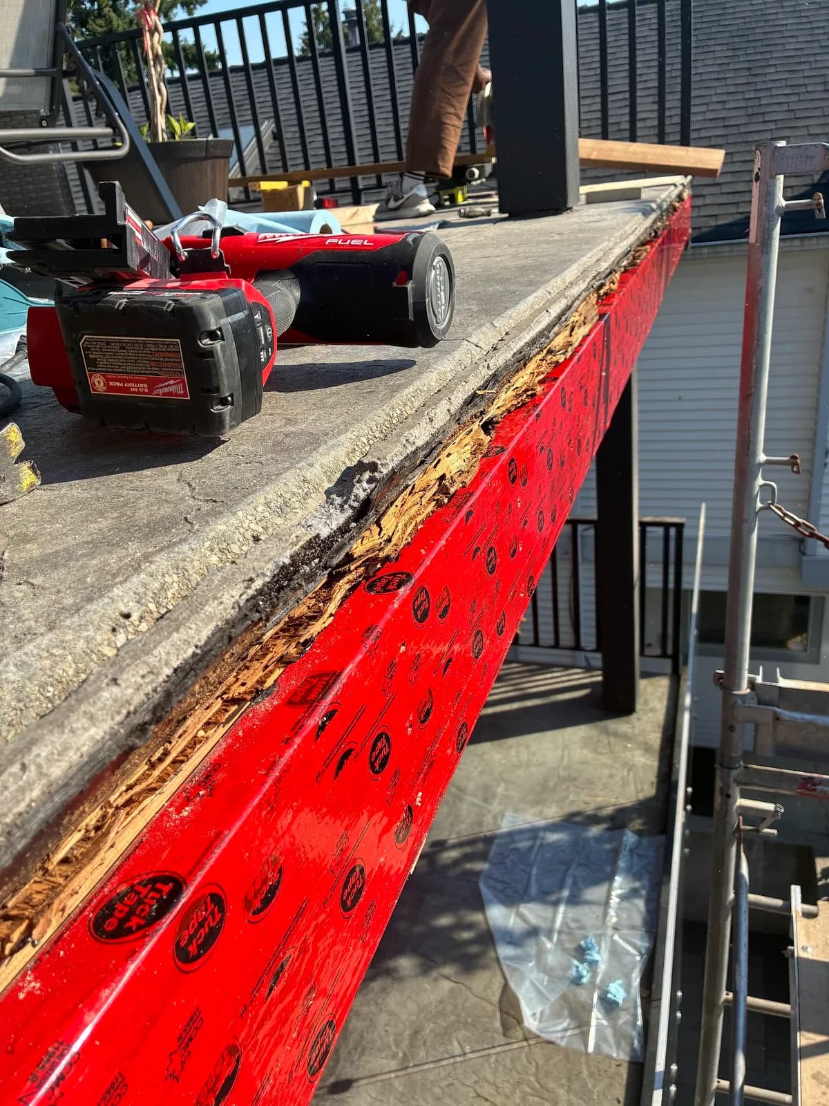 Deteriorated wood exposed along a raised deck edge above red flashing membrane