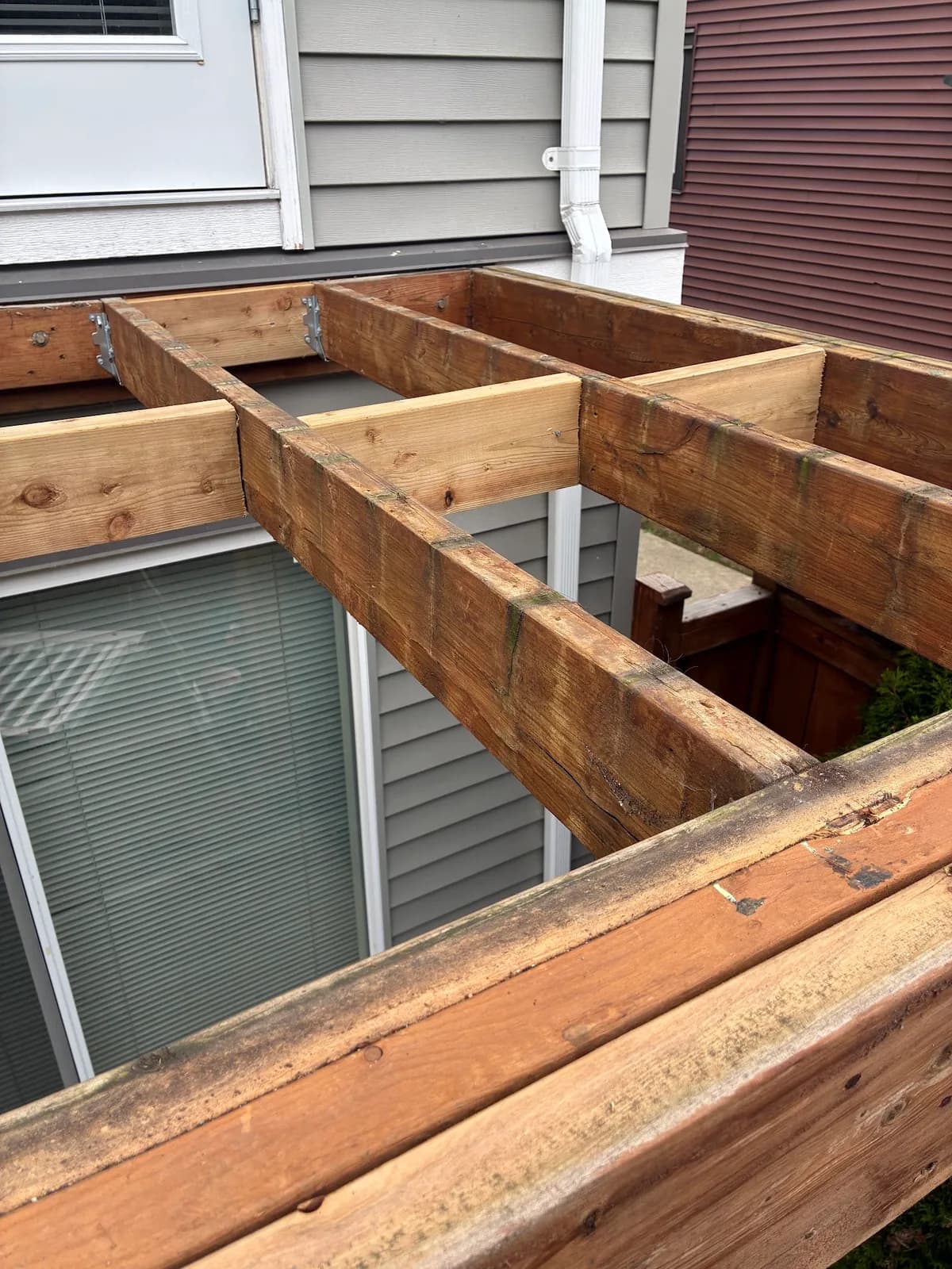 Exposed wood deck joists and perimeter framing beside a sliding patio door