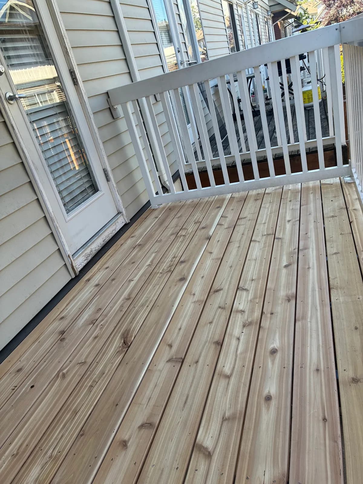 Wood deck surface beside grey house siding and a light grey railing