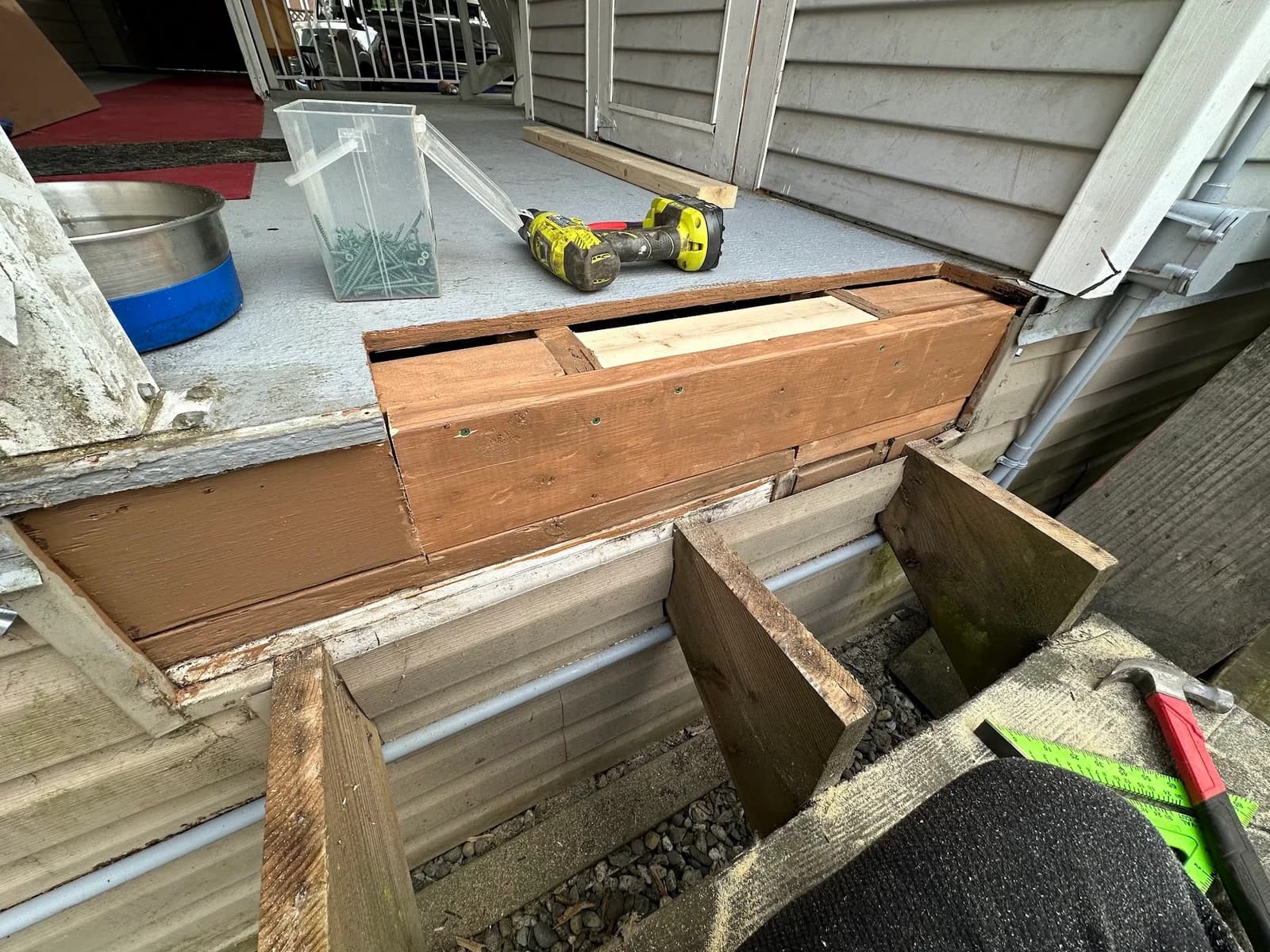 Deck framing exposed at the house wall beneath a patio door during repair work