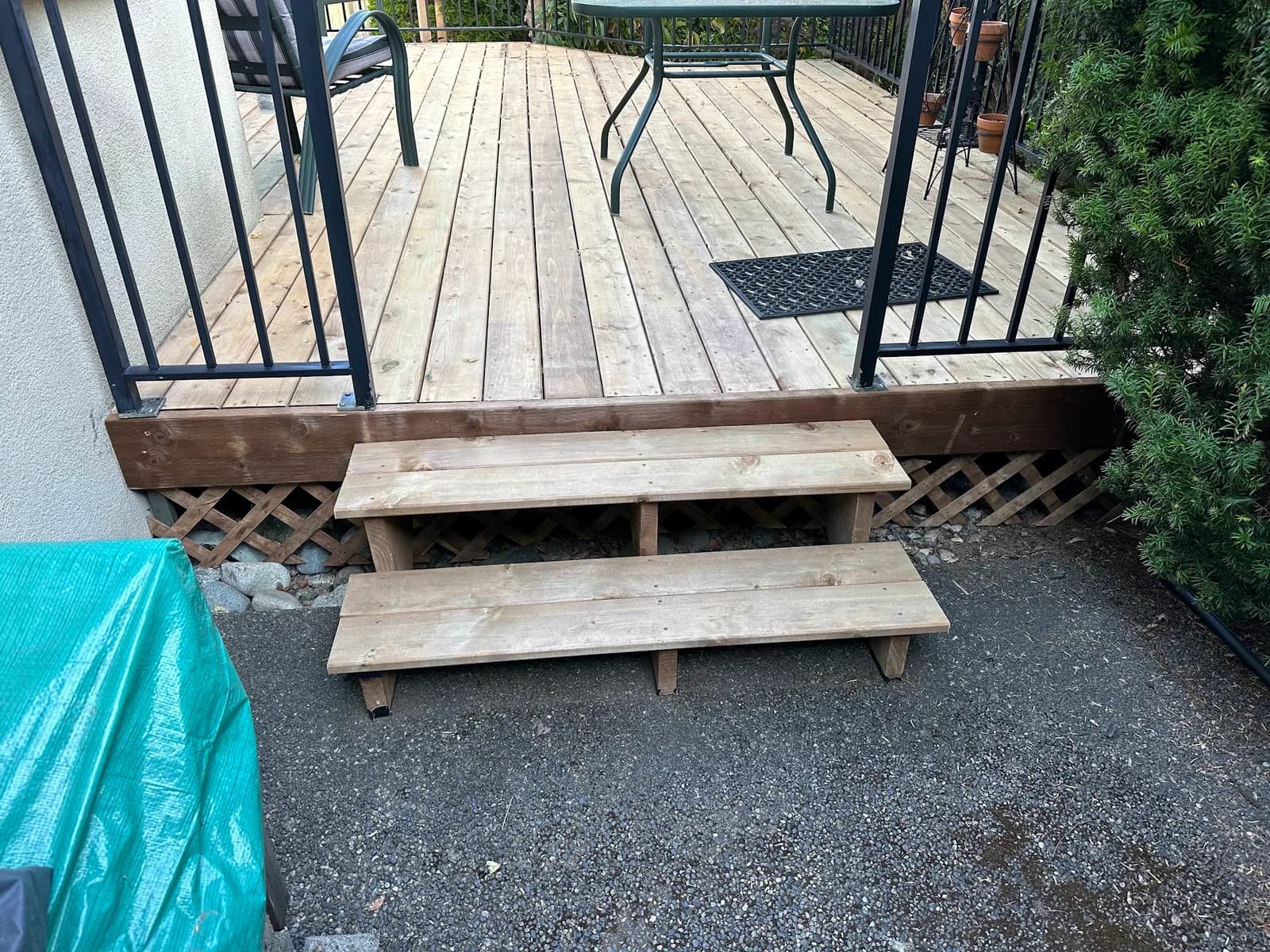 Two wood steps leading from a paved path onto a deck with black railings