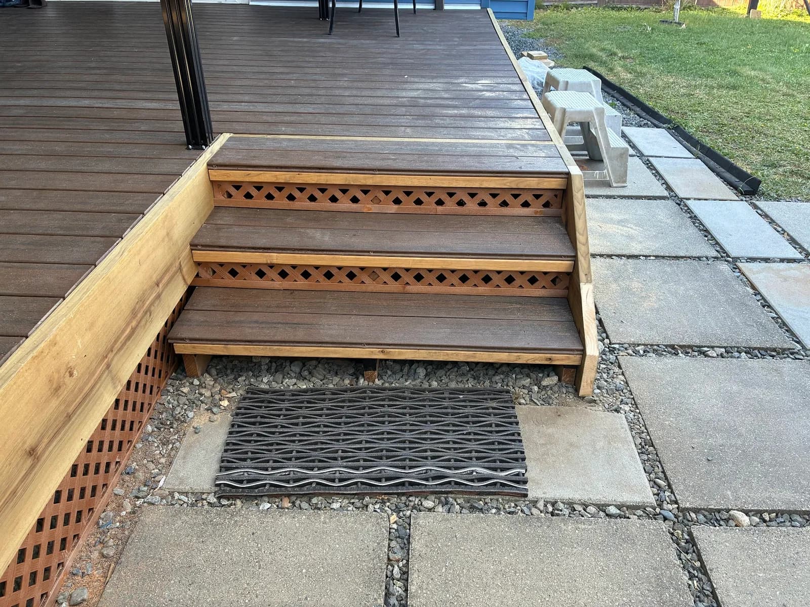 Three brown deck steps with wood trim and lattice risers leading to the patio
