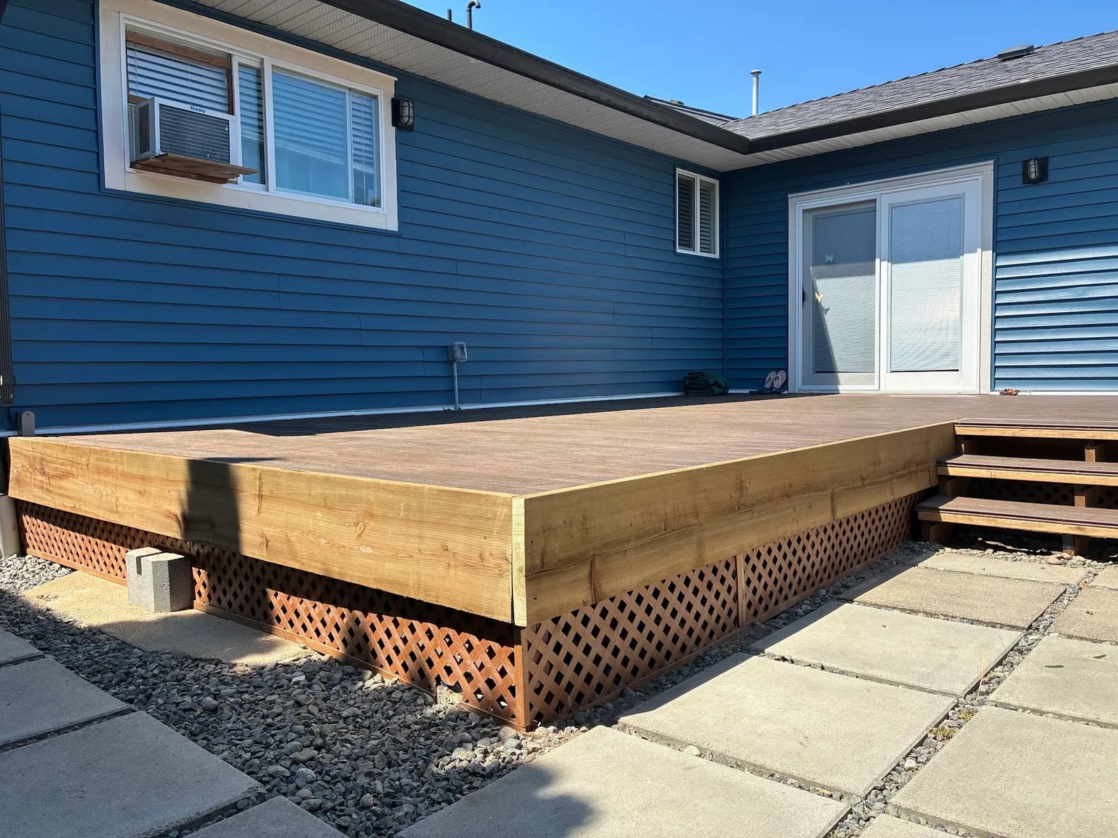 Decking with wood perimeter trim and lattice skirting beside the blue house