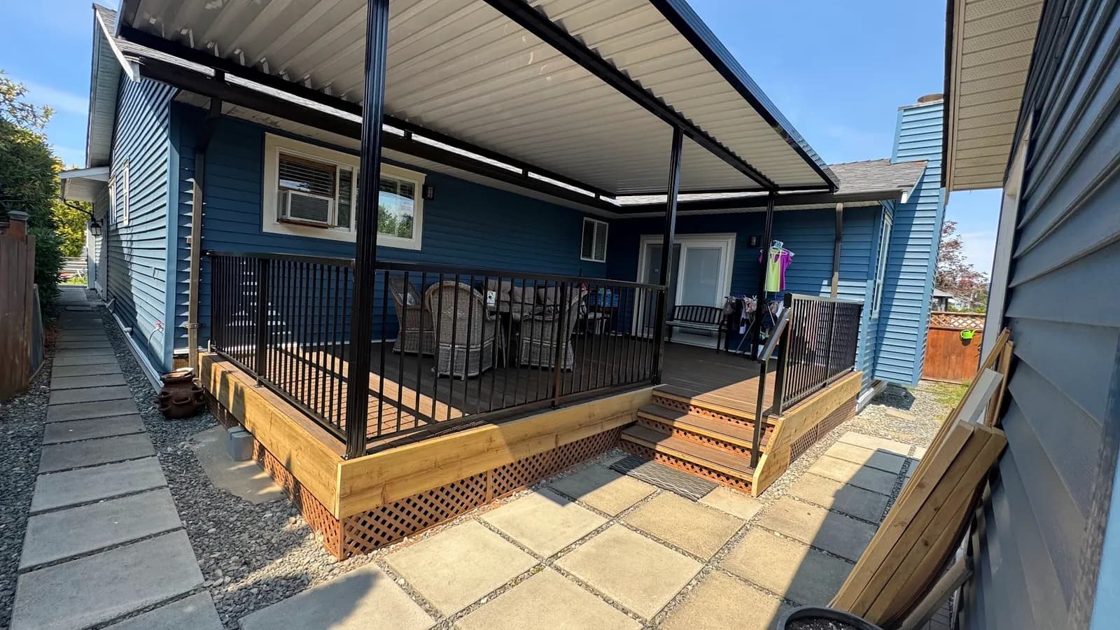 Finished deck with black railings, stairs and wood trim beside a blue house